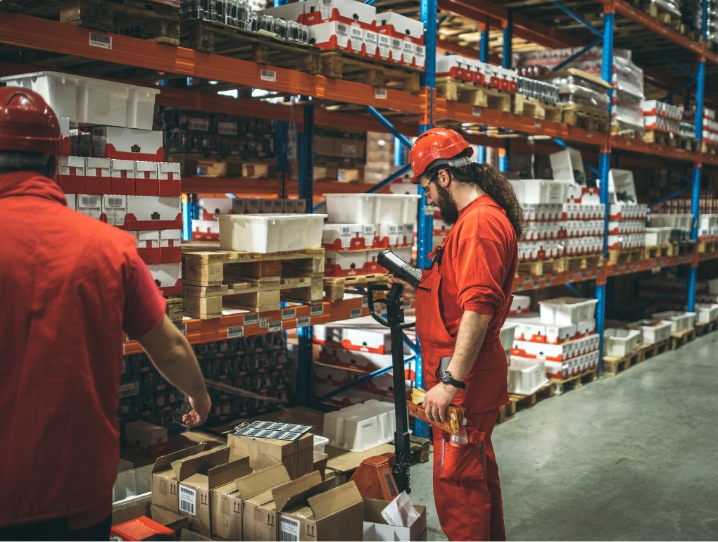 Man in orange suit and hard hat looking at RF scanner in front of inventory shelf